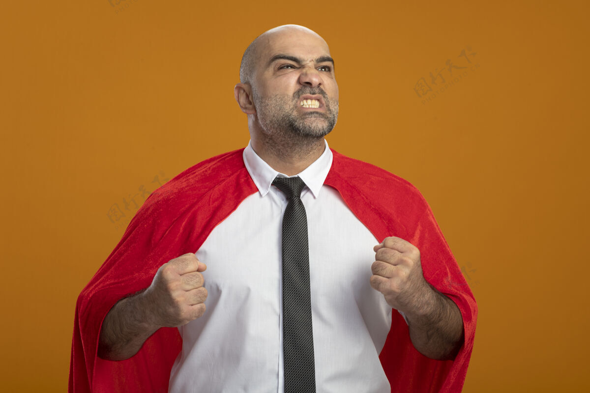 表情身穿红色斗篷的超级英雄商人站在橙色的墙上 一边看一边握紧拳头 表情愤怒 咄咄逼人愤怒人看