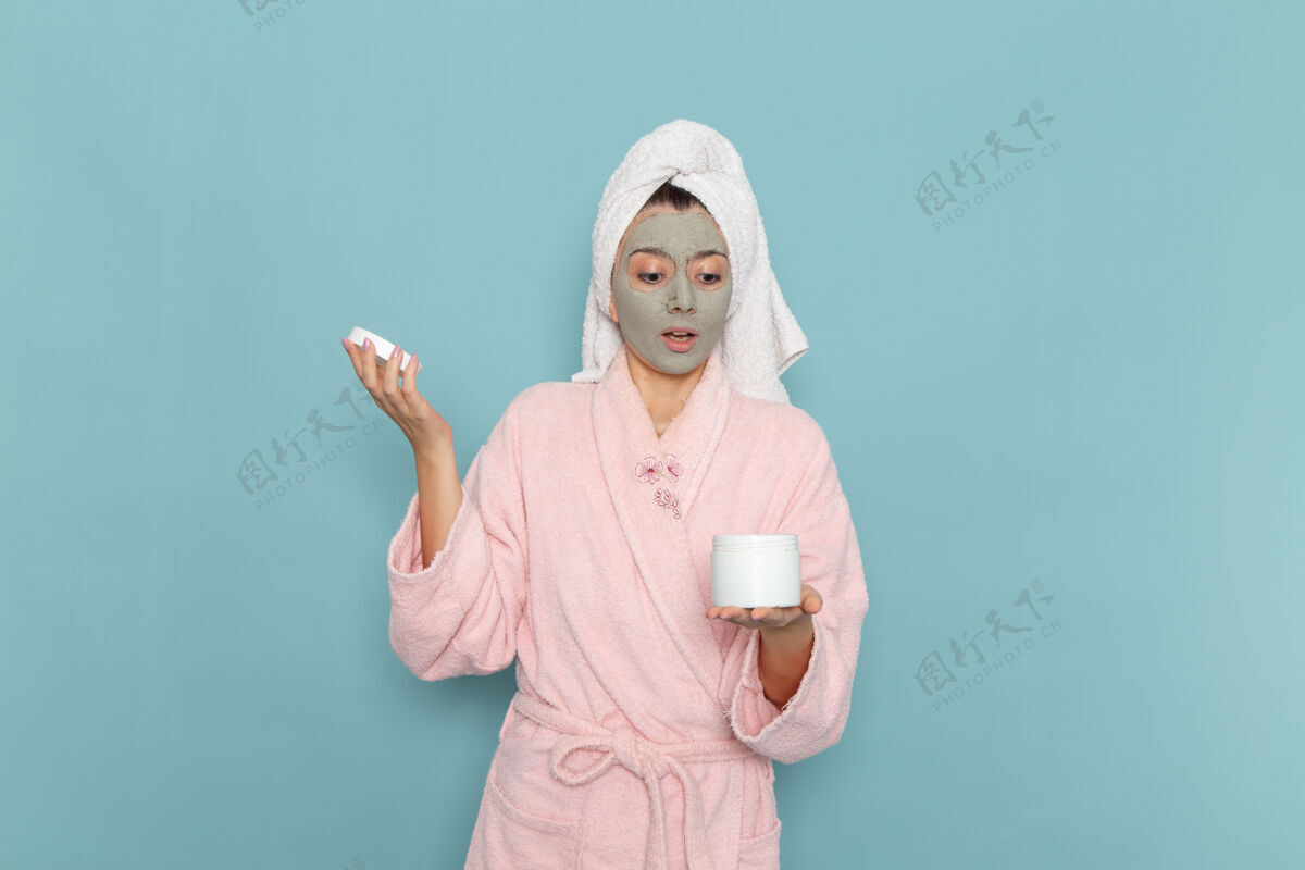 人正面图身着粉色浴袍的年轻女性淋浴后拿着面霜在蓝色墙壁上美丽的水浴面霜自护淋浴浴室人成人浴室