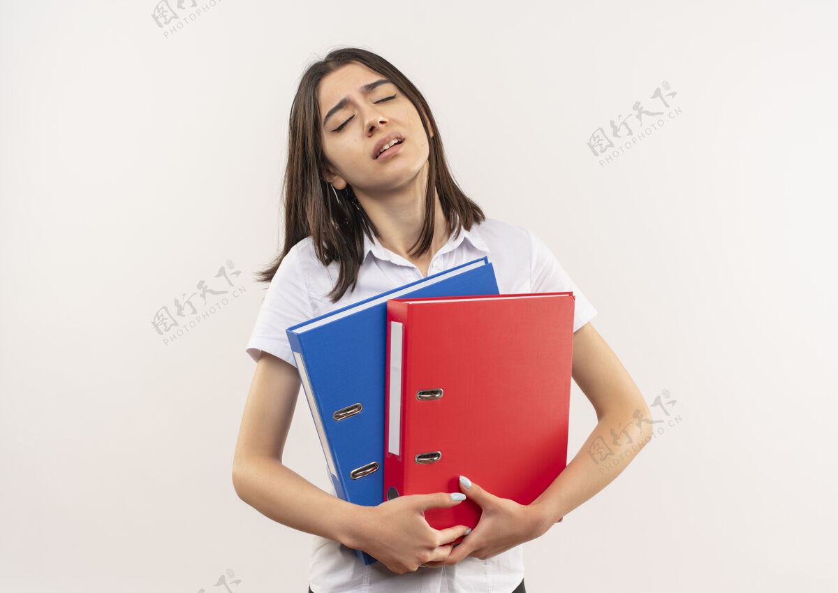 人一个穿着白衬衫的年轻女孩站在白墙上 手里拿着文件夹 看上去又累又无聊人疲惫夹着