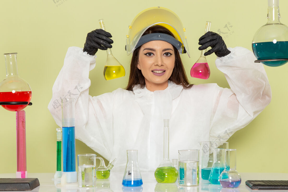医生正面图身着特殊防护服的年轻女性化学家在绿色办公桌上工作化学工作女性科学实验室溶液科学防护