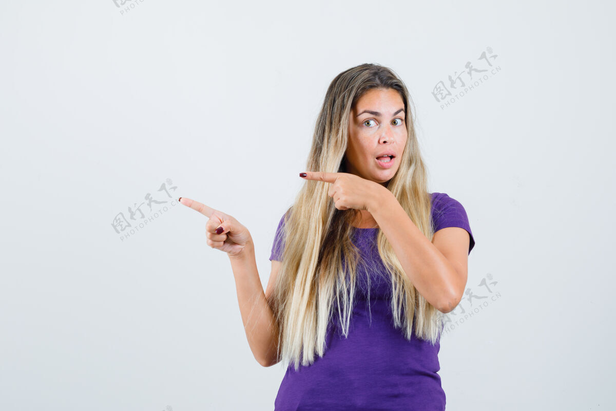 肖像金发女人指着一边 穿着紫色t恤 看上去很好奇前视图看好奇美丽