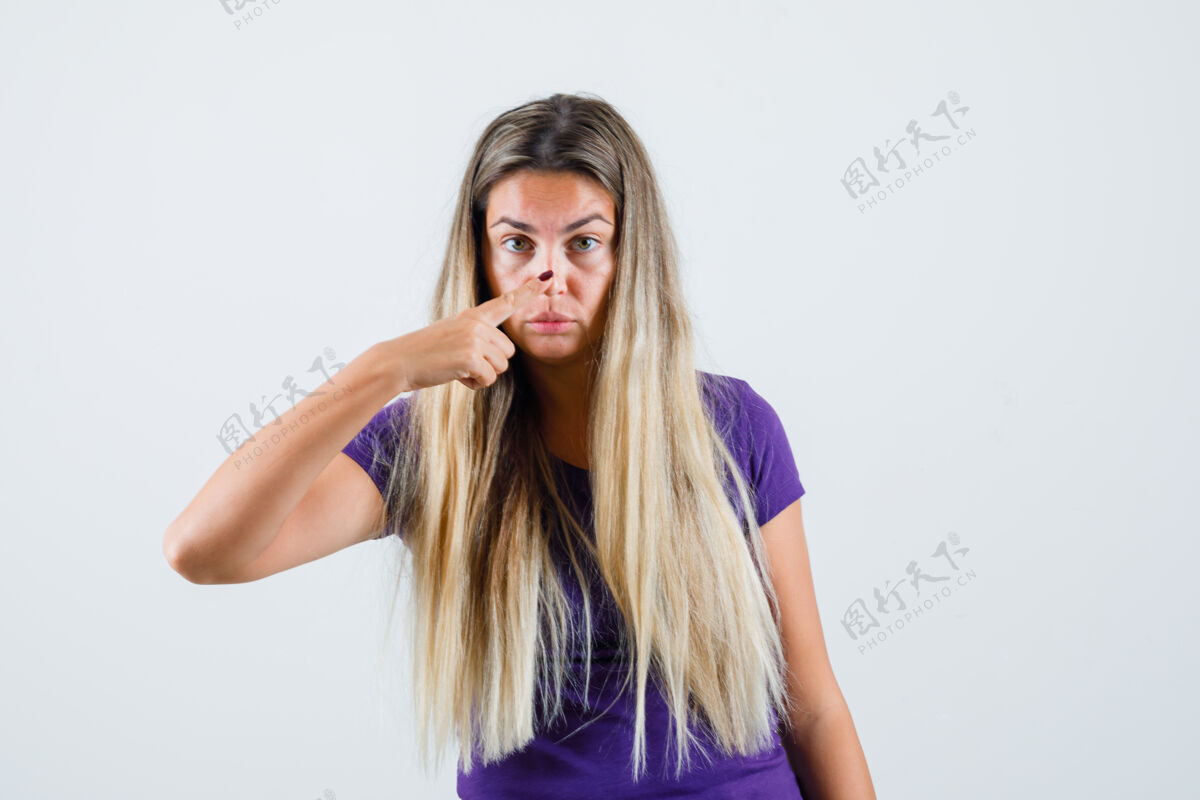 可爱金发女士用手指触摸鼻子在紫罗兰色t恤 前视图长漂亮手指
