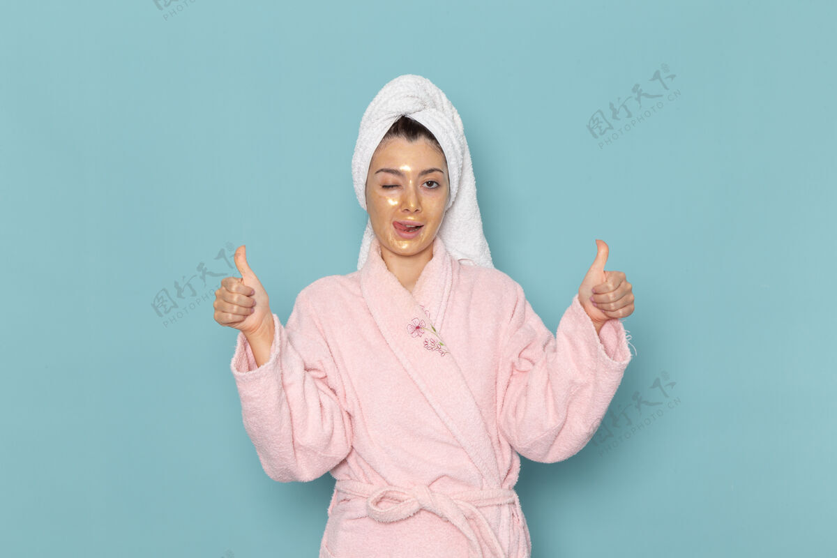 微笑正面图身着粉色浴袍的年轻女性在蓝色墙壁上摆姿势淋浴清洁美容自护霜浴袍人年轻人