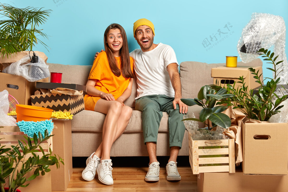 丈夫高兴的夫妻带着幸福的神情 拥抱的同时坐在客厅的沙发上 搬进新家 纸板箱到处乱放搬迁坐着搬家