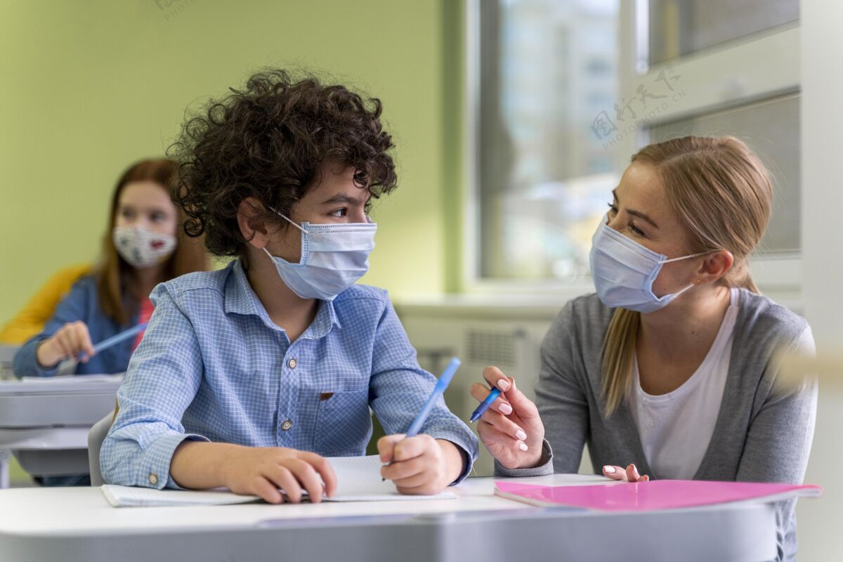 女性戴着医用口罩的女老师在课堂上帮助学生流行病面罩孩子