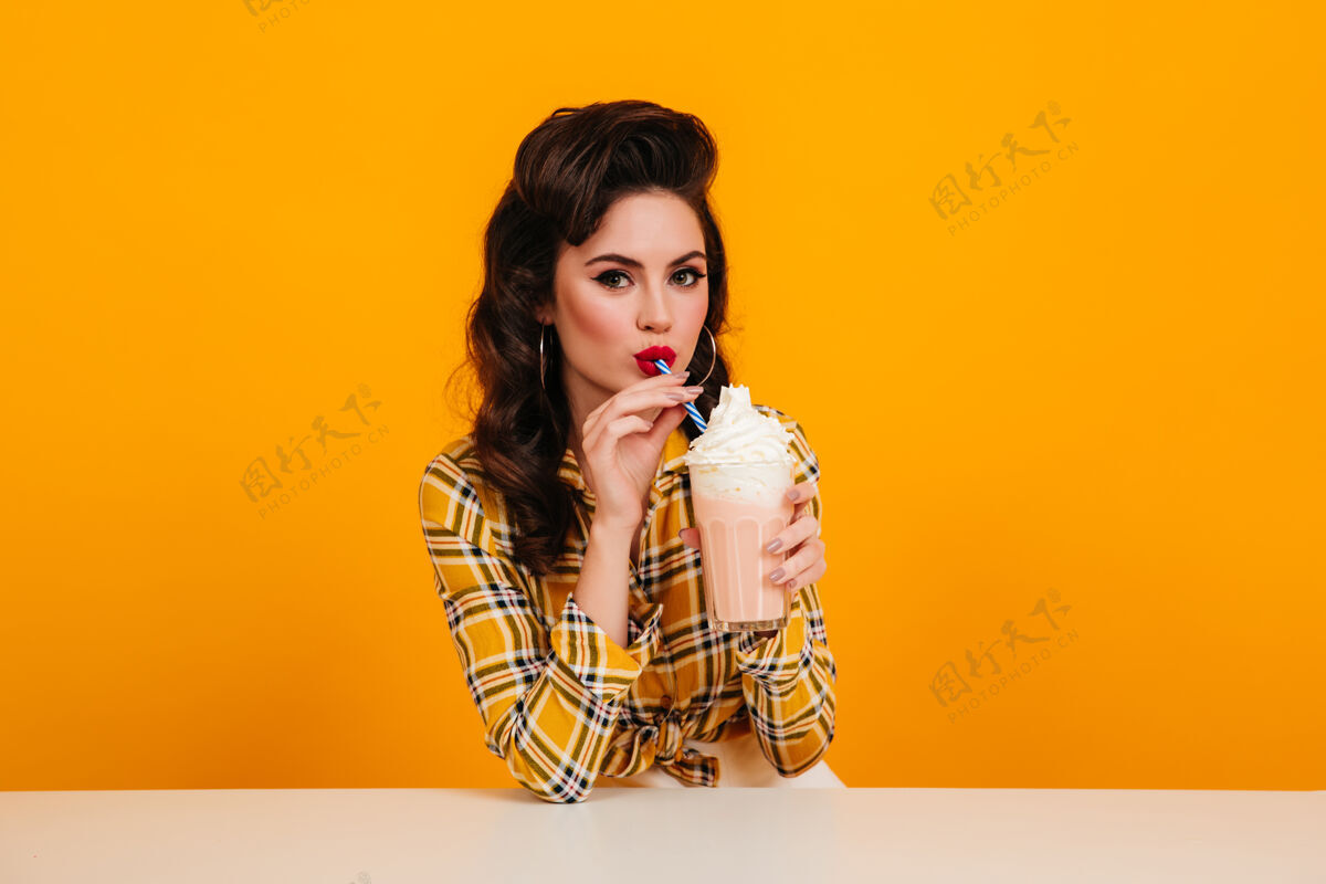 女士性感的欧洲年轻女子喝着奶昔穿着格子衬衫享受鸡尾酒的小女孩的摄影棚照片漂亮脸表情