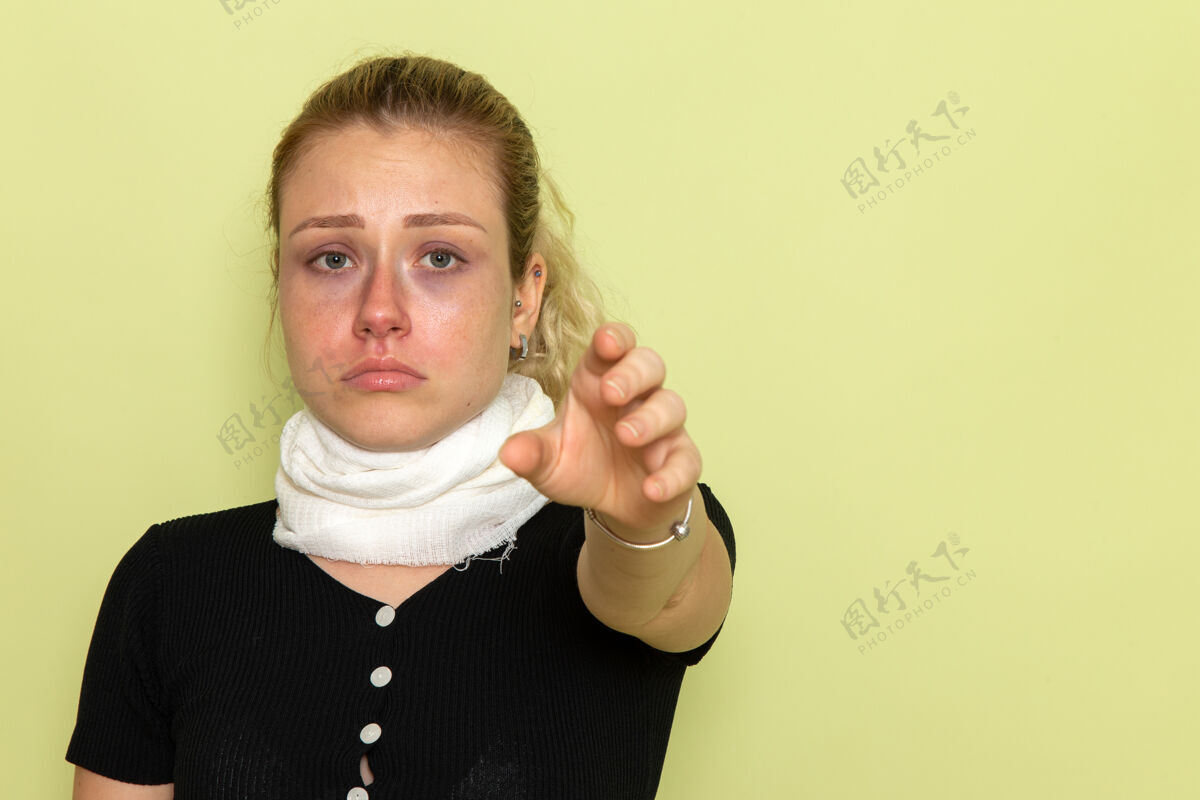 支架正面图年轻女子用白毛巾捂住喉咙 感觉很不舒服 病在淡绿色的墙上 病在女人身上前面毛巾生病
