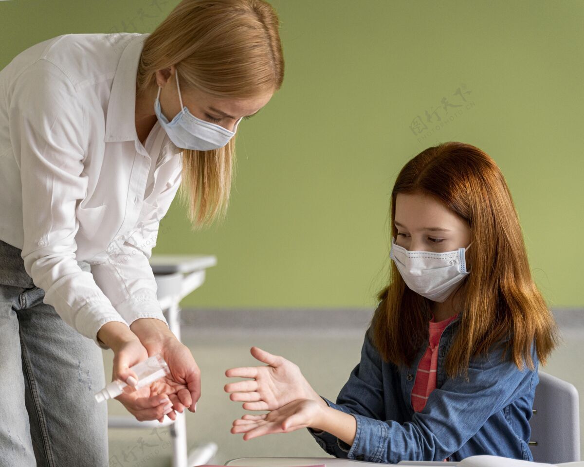 水平老师带着医用口罩在教室里给孩子的手消毒流行病教育新常态