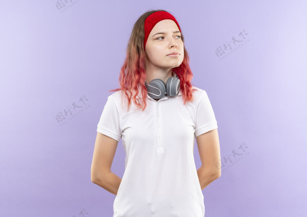 自信戴着耳机的年轻运动女郎站在紫色的墙上 带着自信的表情望向一边耳机女人人
