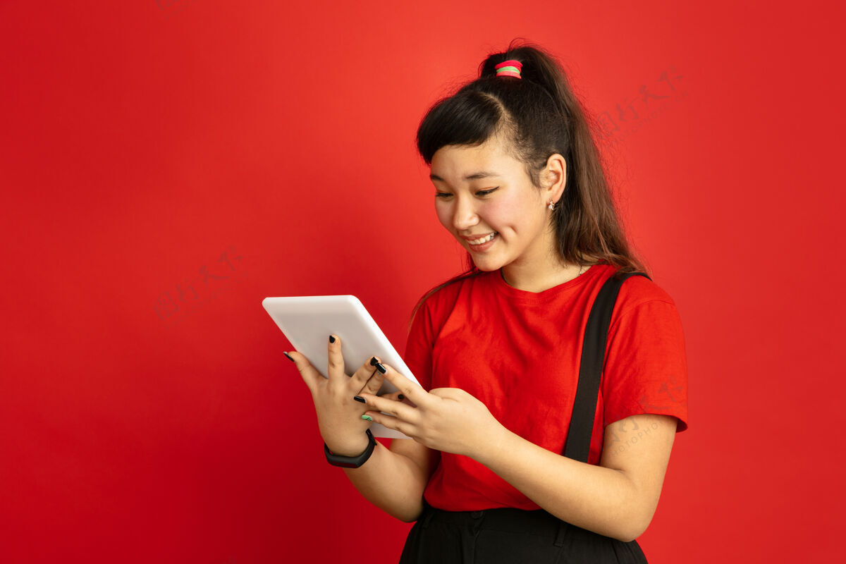 工作亚洲青少年的肖像画被隔离在红色工作室的背景上美丽的深褐色女性模特 留着休闲的长发人类情感的概念 面部表情 销售 广告手持平板电脑表情专业职业