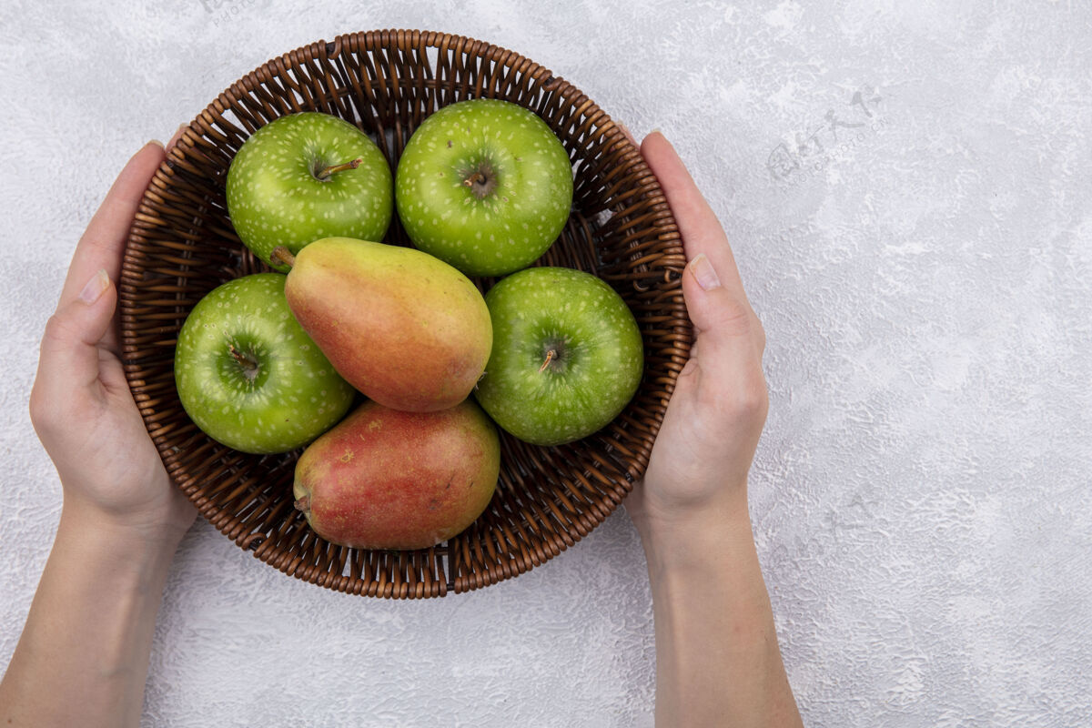 举行俯视图：白色背景下 一个篮子里放着梨子和青苹果的女人景观甜食食物