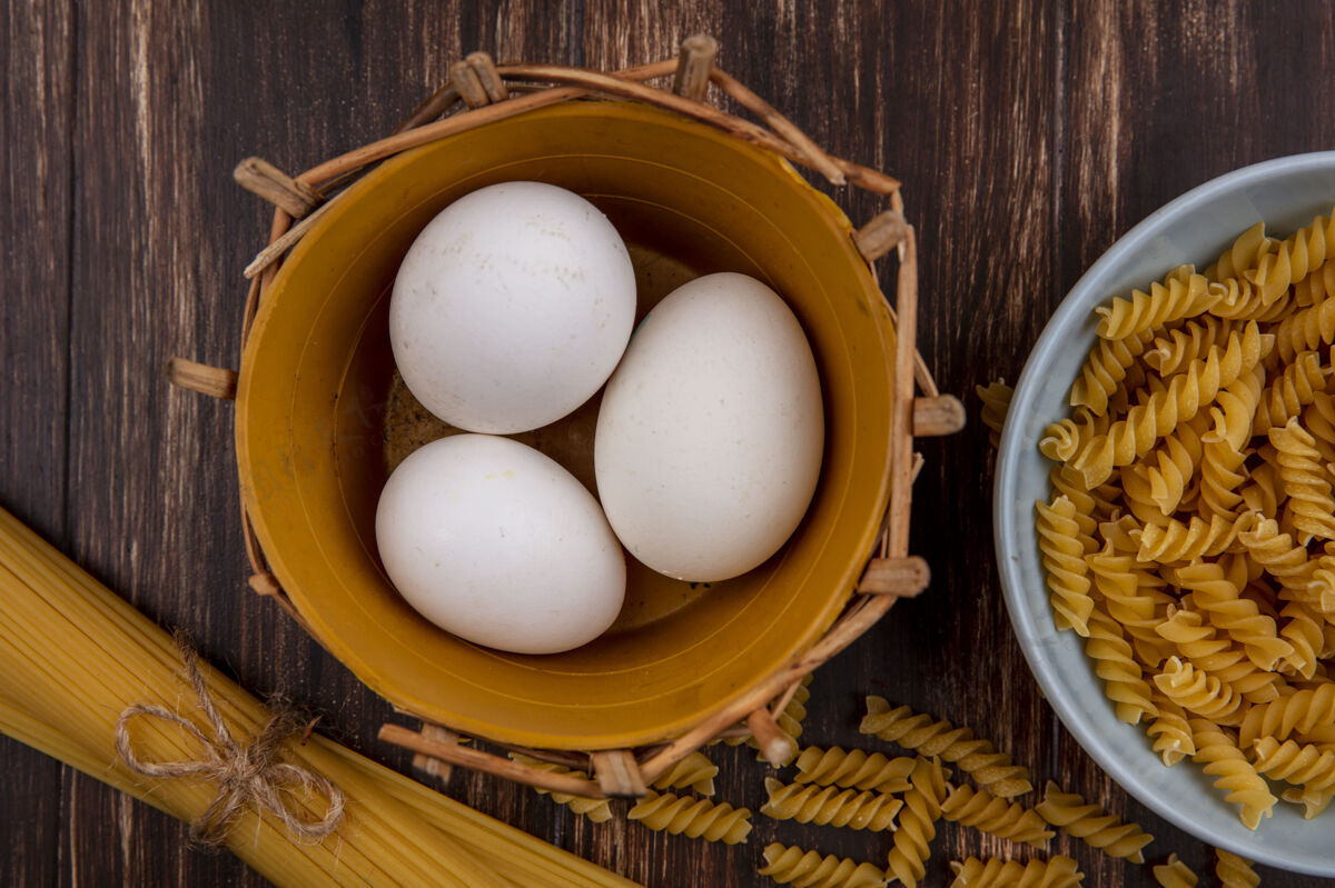 鸡蛋顶视图鸡蛋在篮子里与生意大利面和意大利面在木制背景上营养生的木头