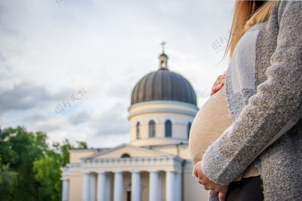 基督教怀孕的女人抱着她的肚子站在基督诞生的大教堂前女人孕妇手