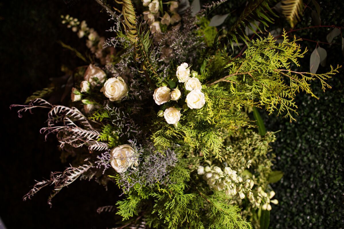 芽高角度拍摄的花束与常绿树叶和白色玫瑰下的灯光自然特写开花