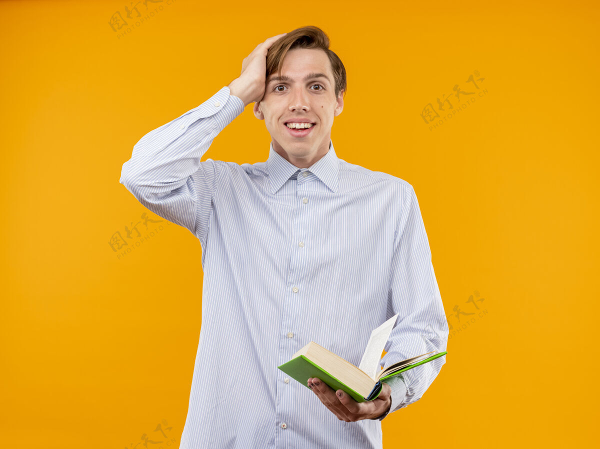 微笑身穿白衬衫的年轻人拿着一本打开的书 站在橙色的墙上 脸上洋溢着惊喜的笑容看着惊喜抱着