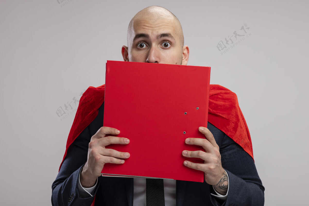 超级英雄超级英雄 留着胡子的商人 穿着红色斗篷 手里拿着一个文件夹遮住脸 站在白色的墙上 惊恐地偷看斗篷文件夹胡须