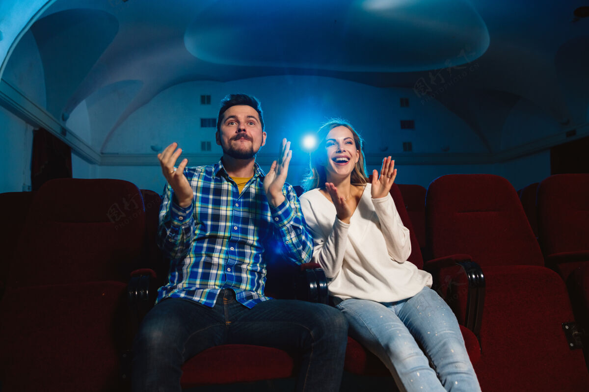 微笑迷人的年轻白种人夫妇在电影院 房子或电影院看电影看起来富于表现力 惊讶和情绪化独自坐着玩关系 爱情 家庭 周末时间坐爆米花电影