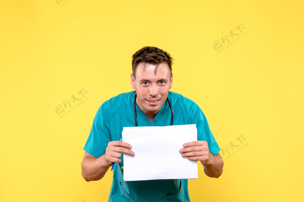 笔记本电脑黄色墙上拿着文件的男医生的正视图文件疾病人