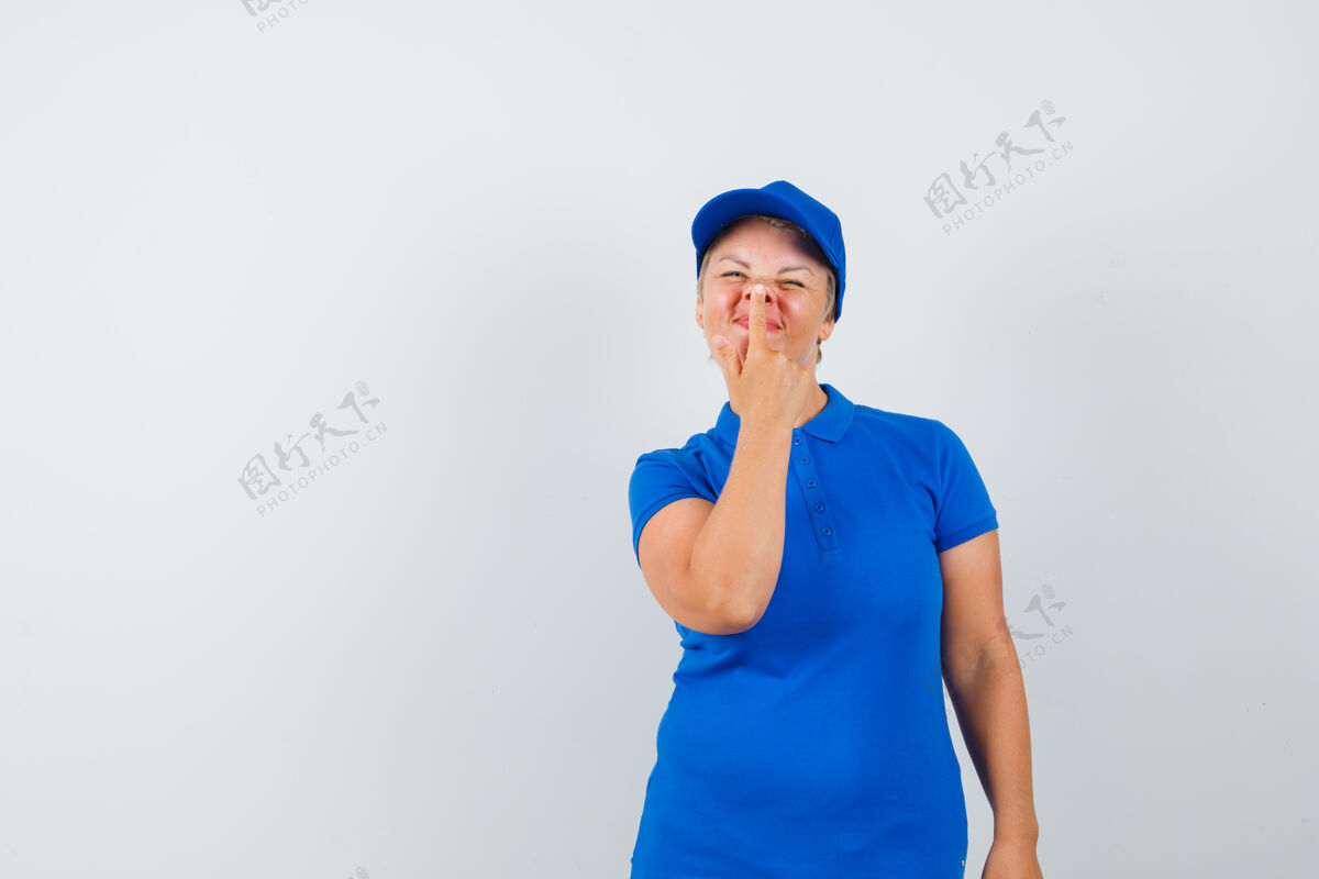 帽子穿着蓝色t恤的成熟女人用手指触摸鼻子 看起来很有趣可爱手指女人
