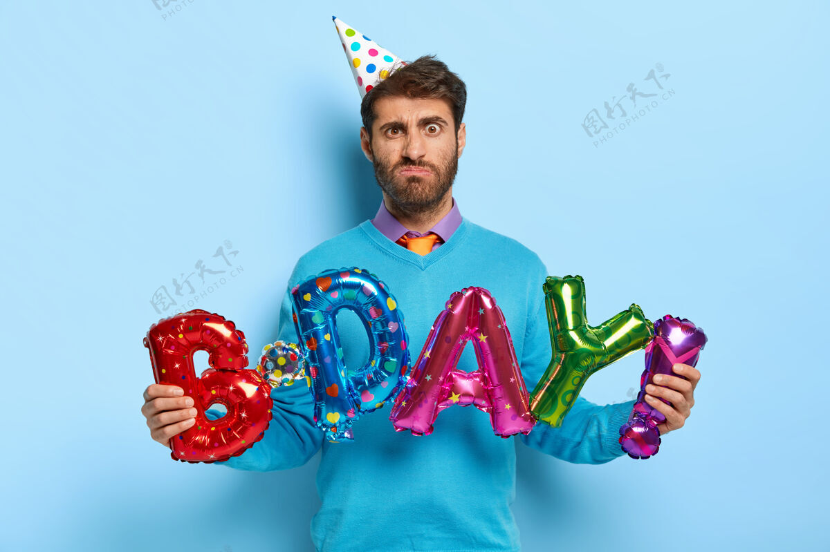 庆祝不满的生日男子手持五颜六色的字母形气球傻笑领带服装