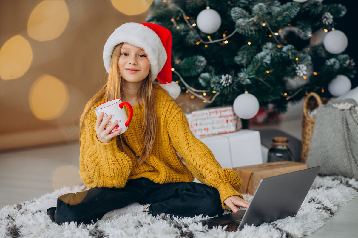 在线可爱的女孩在圣诞树旁用电脑网上商店圣诞销售科技