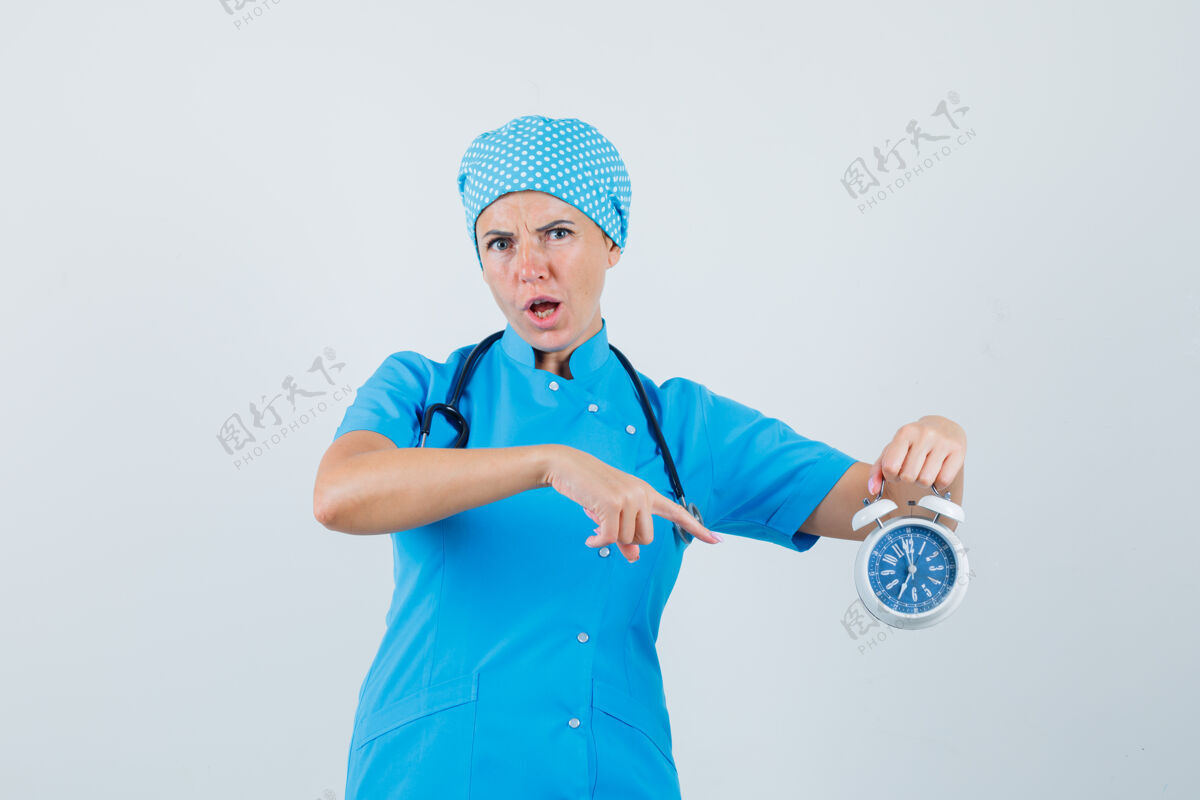 女人女医生指着蓝色制服的闹钟 焦急地看着前视图外科医生职员病人