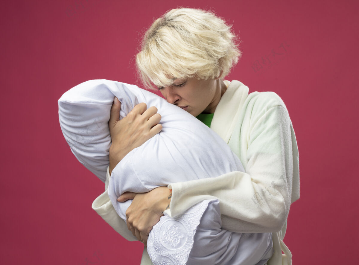 感觉生病的不健康的女人 短发抱着枕头 站在粉红色的背景上 试图闻到枕头的味道 感觉不舒服生病枕头不健康