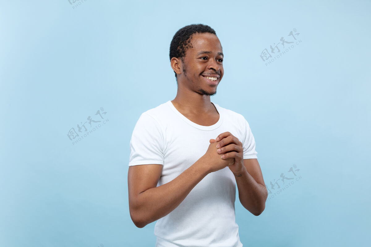 事业身穿白衬衫 蓝色背景的年轻非洲裔美国男模的半身特写肖像人类情感 面部表情 广告概念疑惑 询问 表现不确定性 微笑公司男人非洲