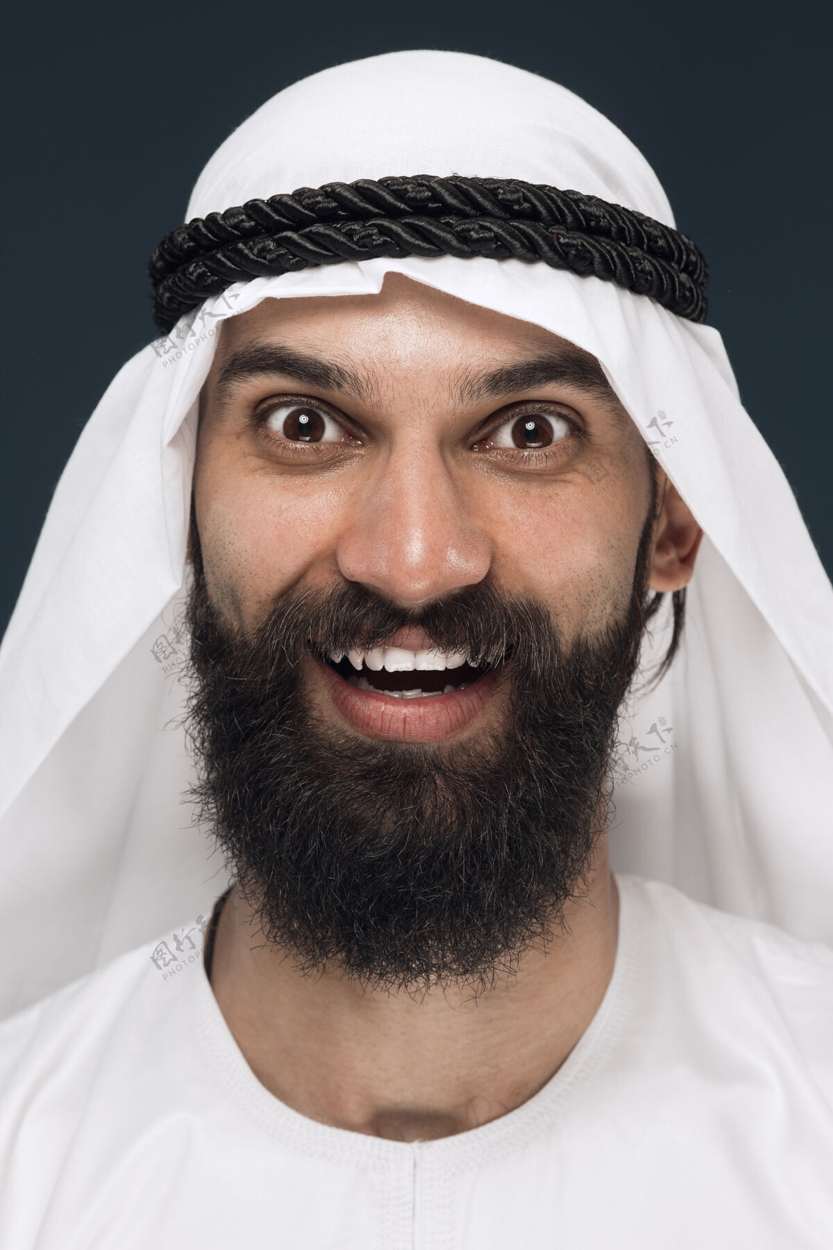 惊讶深蓝色工作室背景上的阿拉伯沙特商人特写肖像年轻的男模站着微笑 看起来很快乐商业概念 金融 面部表情 人类情感惊奇阿联酋成人
