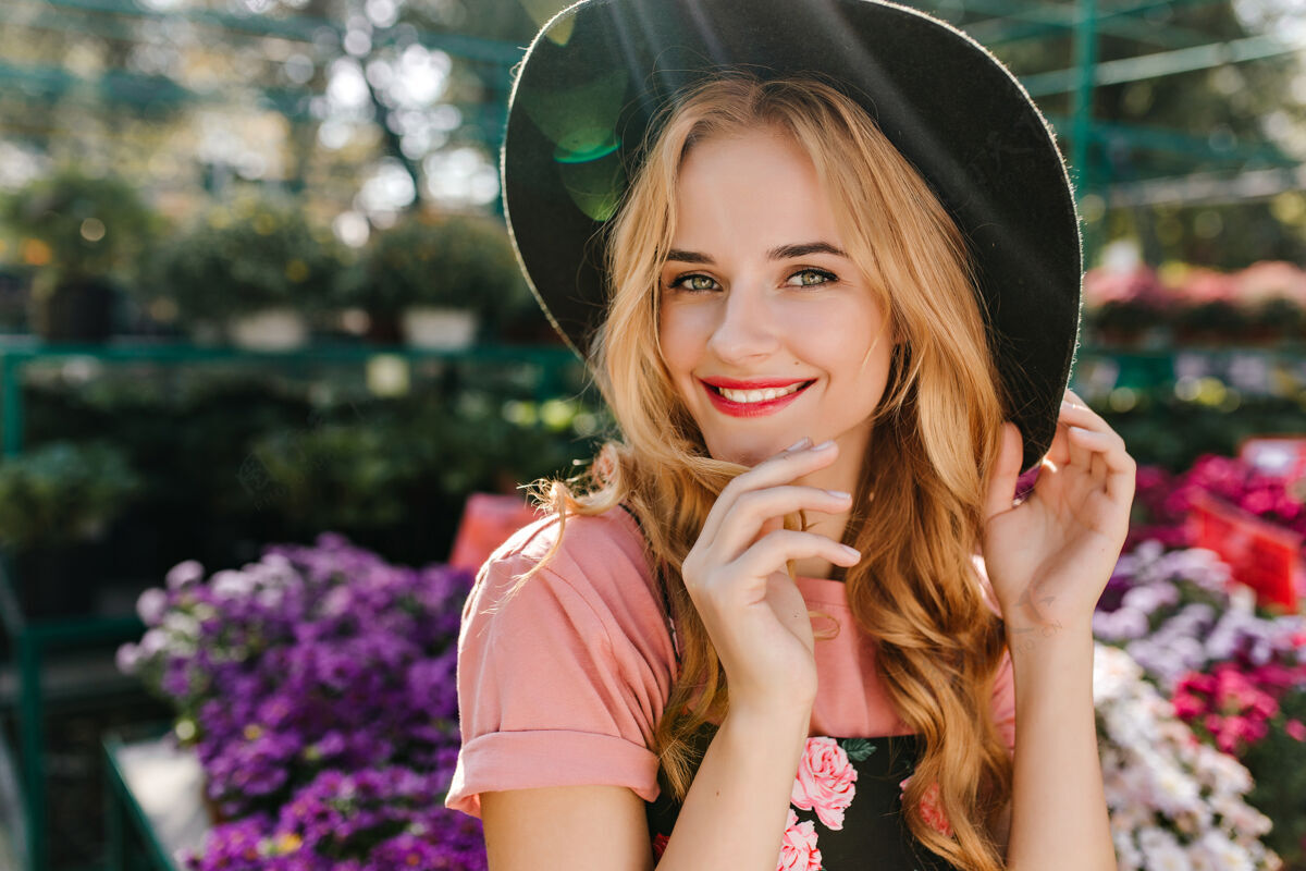 玫瑰心醉神迷的年轻女子 眼睛明亮 在花丛旁摆姿势可爱的欧洲女子 戴着帽子 在橘子园里冷藏温室脸花束