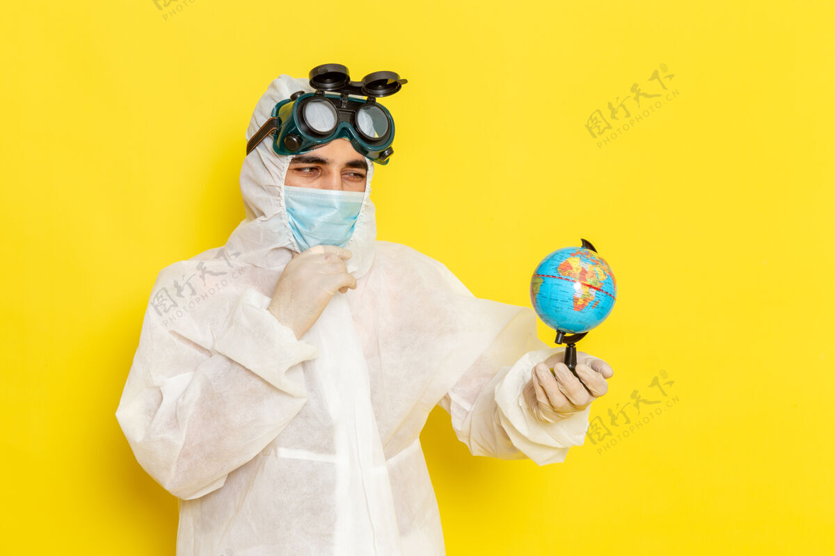 前正面图：一位身着特殊套装的男科学工作者 在黄色的办公桌上拿着小地球仪思考男科学实验服