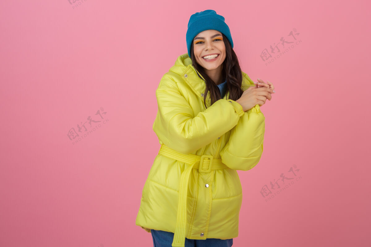微笑迷人活跃的女人穿着鲜艳的黄色冬季羽绒服在粉色墙壁上摆造型 笑容可掬 温暖的外套时尚潮流 疯狂惊艳的表情寒冷女孩季节