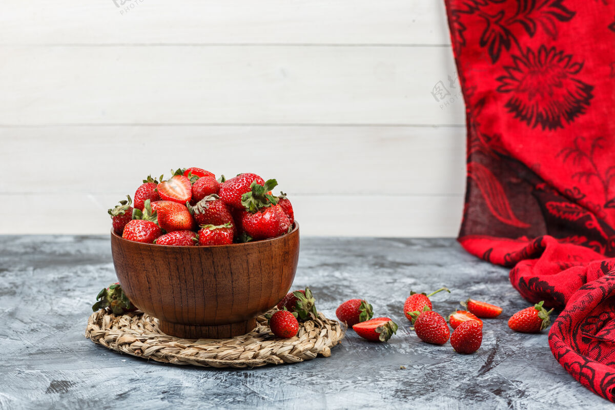 柳条把一碗草莓放在圆形柳条垫子上 在深蓝色大理石和白色木板表面用红领巾围起来水平的自由空间放你的文字碗食物桌子