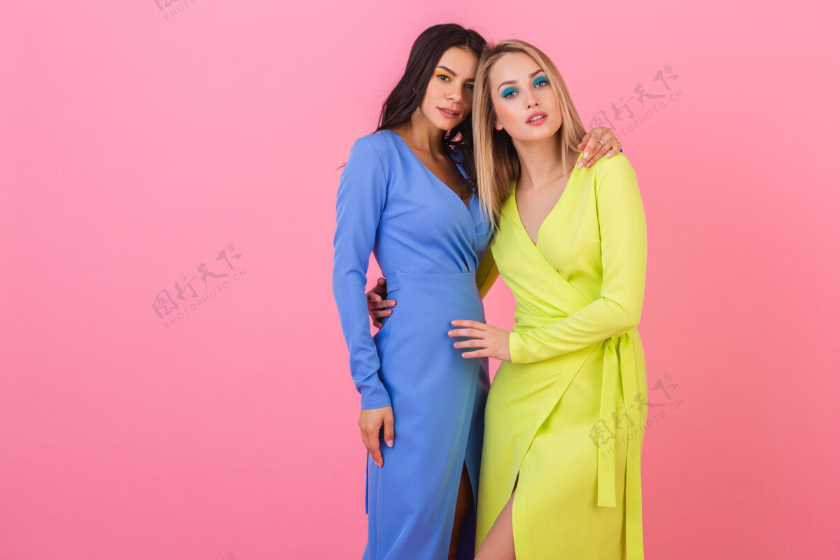 衣服两位时尚性感的女士身着蓝黄相间的时尚多彩礼服 在粉色墙面上摆造型 春日时尚潮流衣服折扣春天
