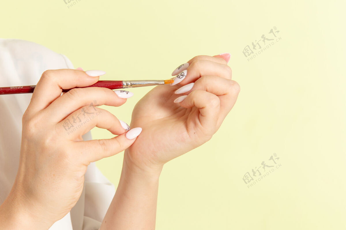 美容师正面图年轻漂亮的女性穿着白衬衫 指甲在绿色的表面上工作手指女性指甲