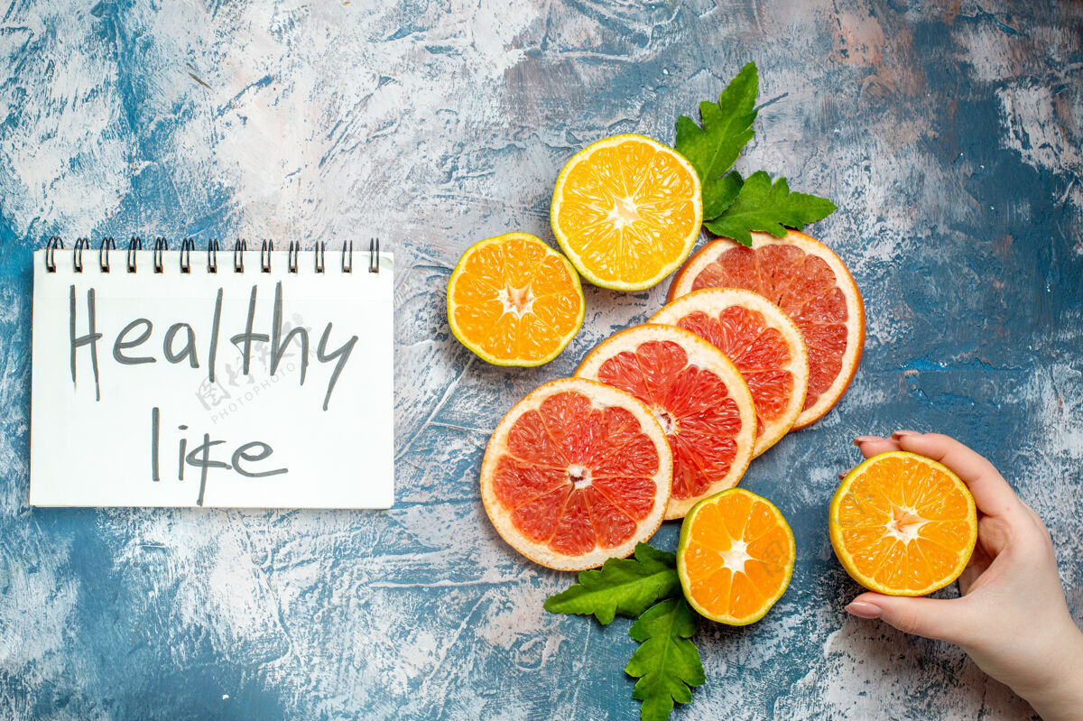 葡萄柚俯瞰健康生活写在记事本上切橘子和柚子女手拿着切普通话在蓝白色的表面健康生活顶部写作