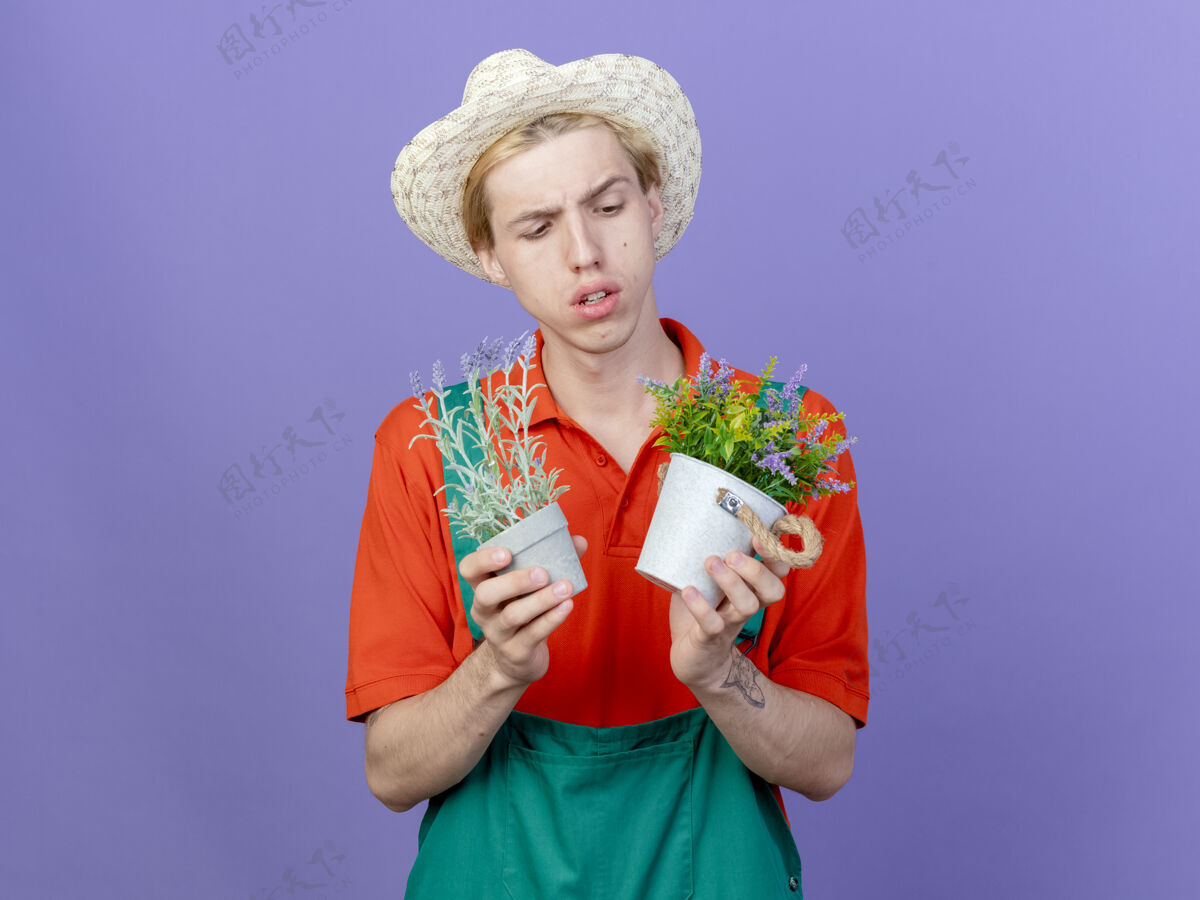 使年轻的园丁 穿着连体衣 戴着帽子 手里拿着盆栽植物持有立场不确定