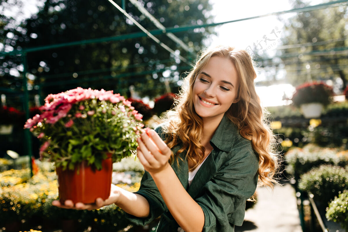 爱好一位金发碧眼 笑容温柔的年轻女子 身着绿色长袍 系着腰带 正在温室里工作开花成人玫瑰