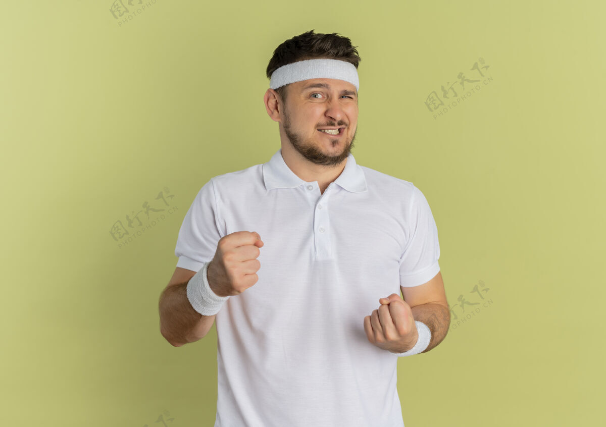 年轻身穿白衬衫 头箍 握紧拳头的年轻健身男子站在橄榄墙外 神情迷茫健身男人运动