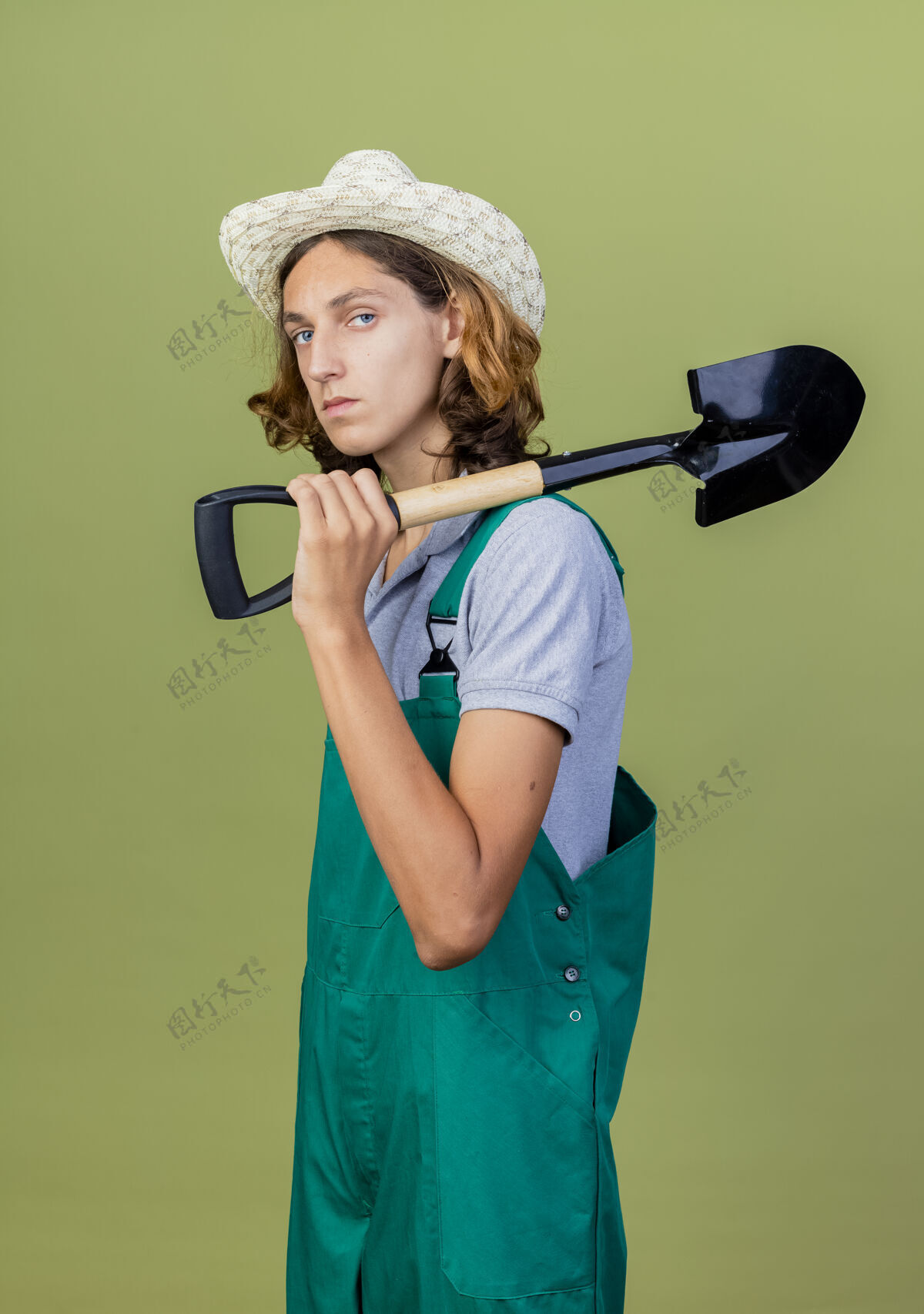站着年轻的园丁穿着连体衣戴着帽子拿着铲子帽子抱着年轻