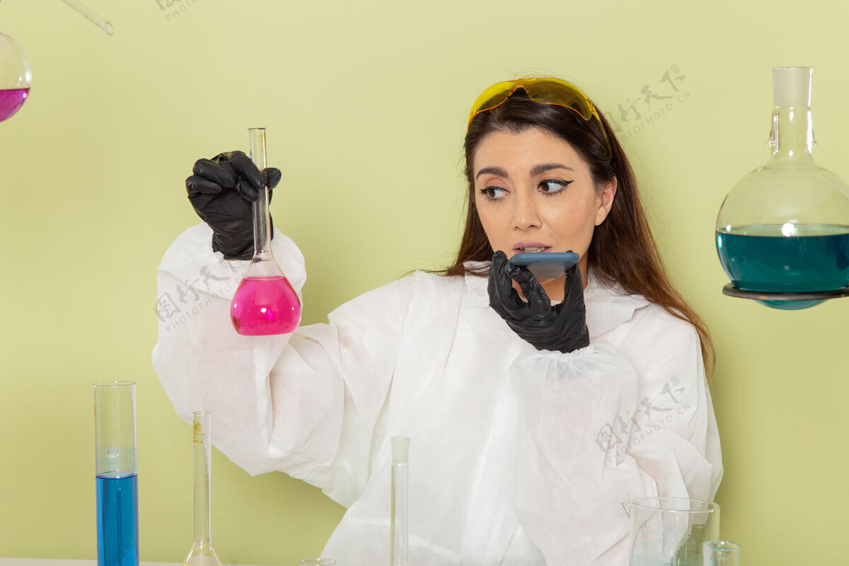 实验室正面图穿着特殊防护服的女化学家拿着绿色表面上有粉红色溶液的烧瓶烧瓶专业化学品