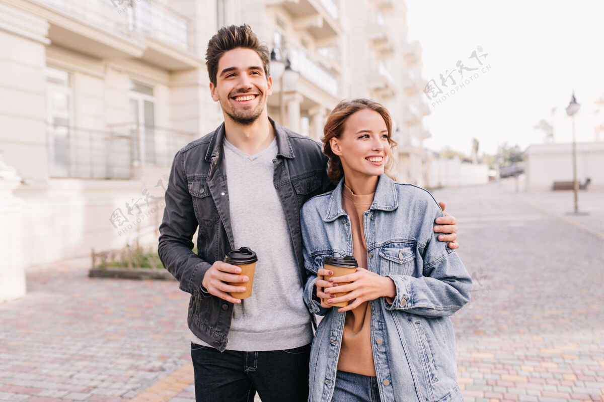 城市帅气的年轻人端着一杯咖啡 拥抱着女朋友笑眯眯的情侣享受着户外约会快乐丈夫卡布奇诺