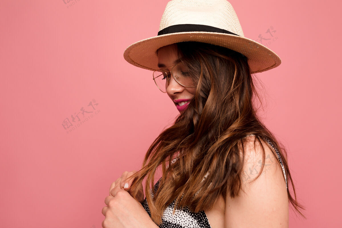 女士戴着帽子和眼镜的时髦欧洲女人在粉红色的墙上摆姿势化妆成功笑
