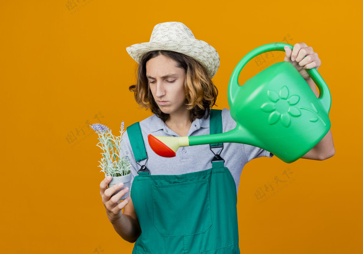 帽子年轻的园丁 穿着连体衣 戴着帽子 手里拿着水罐和盆栽植物植物花年轻