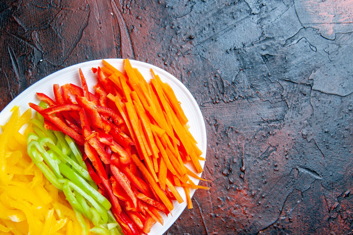 顶部顶视图彩色切辣椒在白色的盘子上暗红色的桌子上复制空间晚餐菜肴胡萝卜
