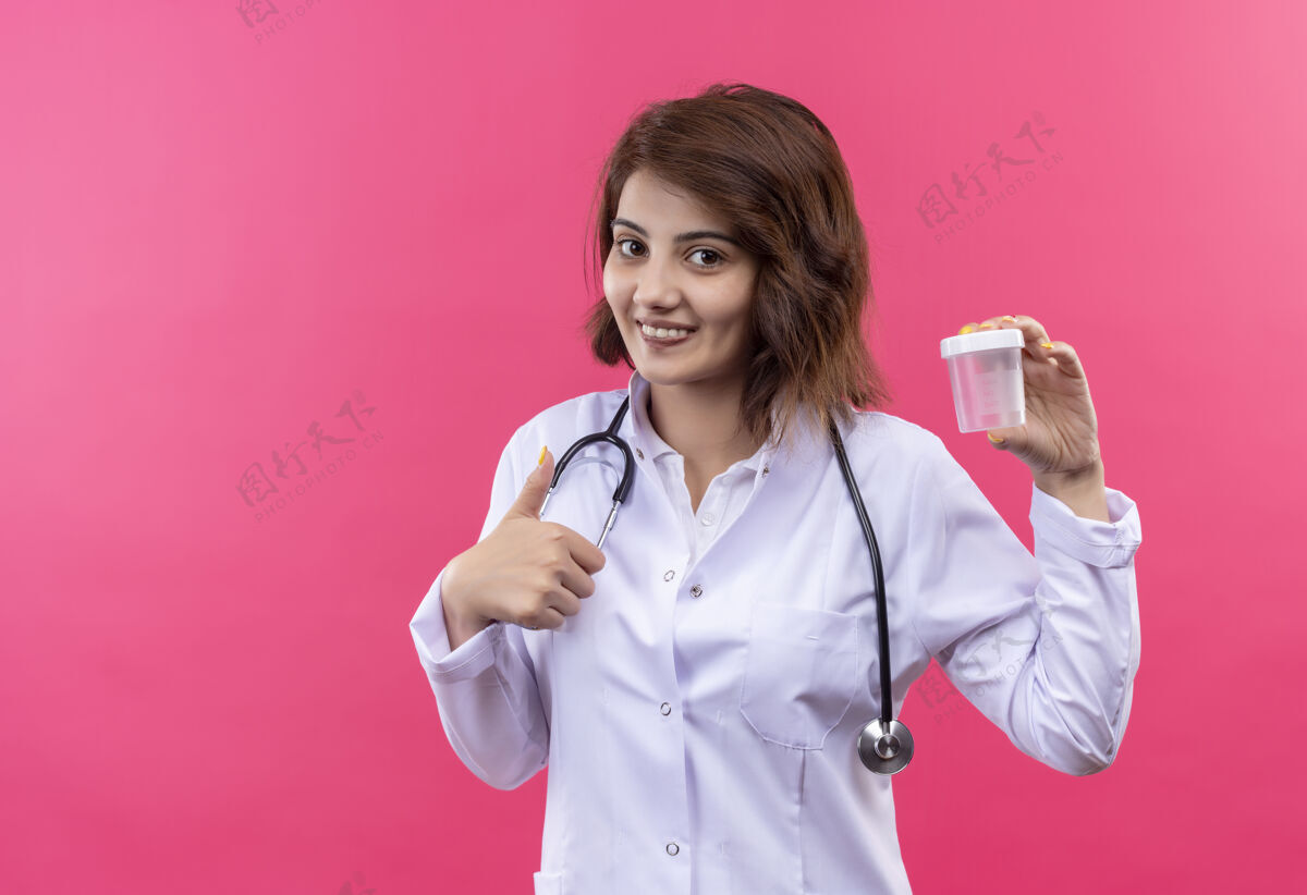 女人身穿白大褂的年轻女医生拿着听诊器 兴高采烈地笑着竖起大拇指听诊器展示微笑