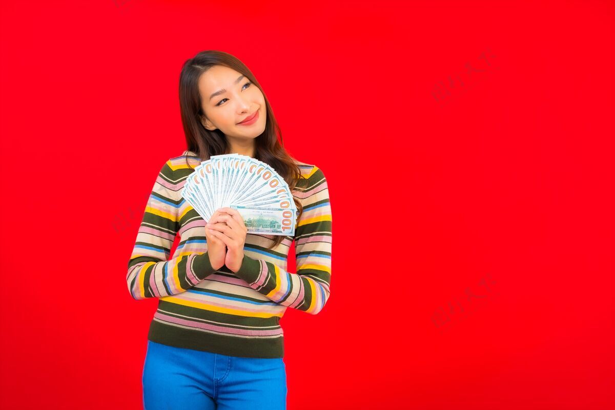 亚洲在红墙上画一幅美丽的亚洲年轻女子的画像 她手里拿着现金和手机赢家成功持有