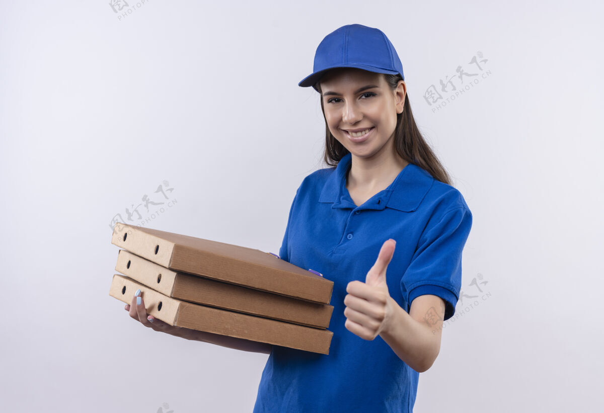 女孩身穿蓝色制服 头戴鸭舌帽的年轻送货员拿着一叠比萨饼盒 脸上带着自信的微笑 竖起大拇指 看着镜头拇指微笑帽子