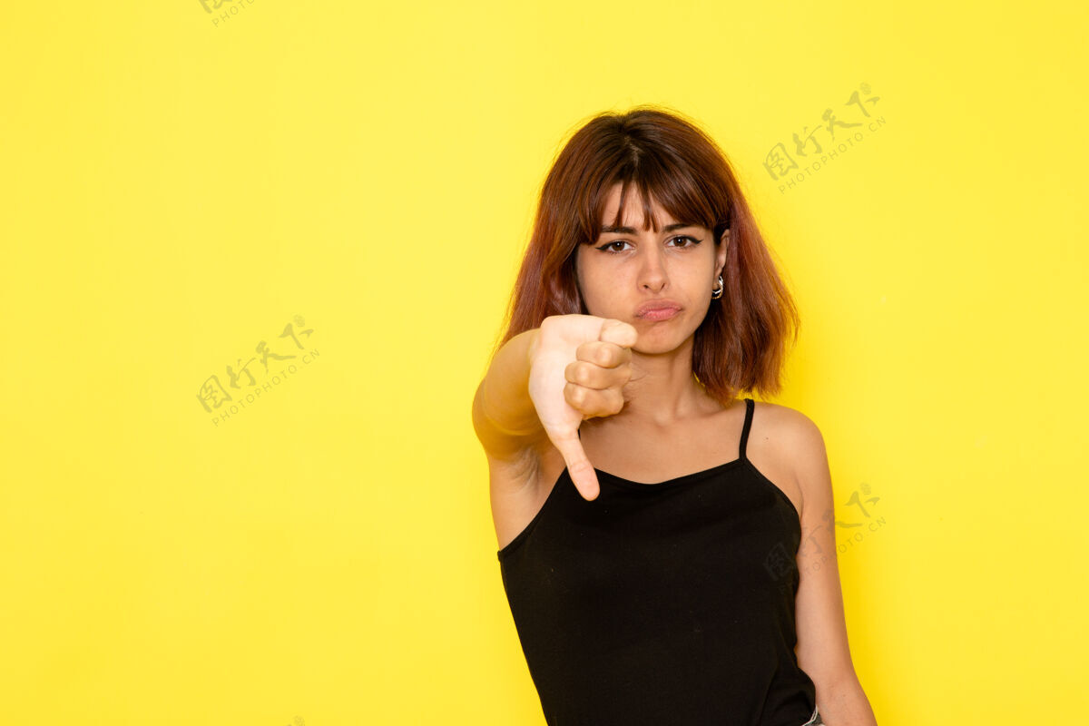 展示身穿黑色衬衫的年轻女性的正面视图 在淡黄色的墙上显示出不同的标志姿势女性漂亮