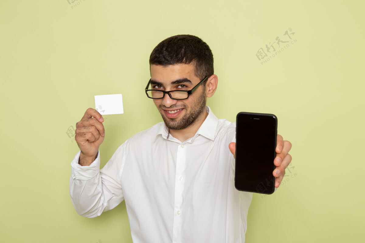 工作身穿白衬衫 手持智能手机和卡片的男性上班族在浅绿色墙上的正视图浅绿色衬衫前面